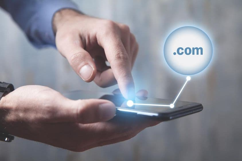 Férfi okostelefont használ egy .com domain gombbal.